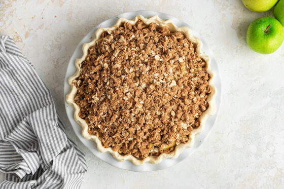 Oat crumble topping added to apples in pie plate.