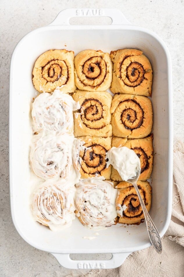 A baking dish with gluten-free cinnamon rolls partially frosted with a cream cheese frosting.