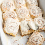 Gluten-free cinnamon rolls in a baking dish topped with a cream cheese frosting.