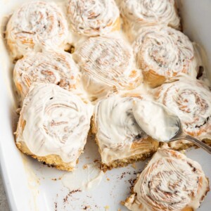 Gluten-free cinnamon rolls in a baking dish topped with a cream cheese frosting.