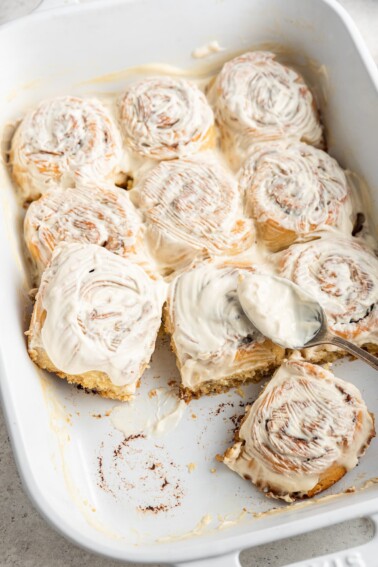 Gluten-free cinnamon rolls in a baking dish topped with a cream cheese frosting.