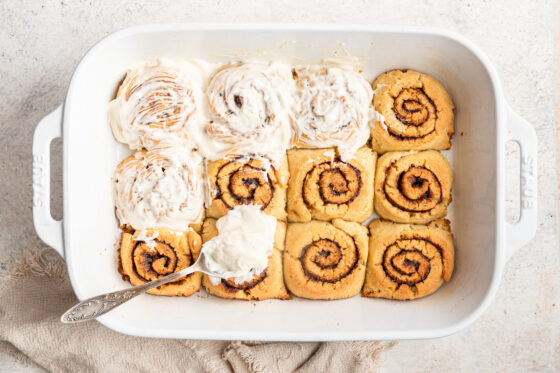 Baked gluten-free cinnamon rolls partially covered with cream cheese frosting.