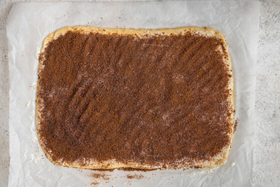 Gluten-free cinnamon roll dough shaped into a rectangle, covered in a layer of butter and cinnamon sugar mixture.