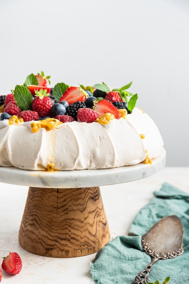 A pavlova topped with coconut whipped cream and fresh fruit on a cake stand.