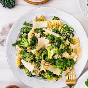 Tuna, broccoli and kale caesar pasta salad on a plate topped with shaved parmesan.