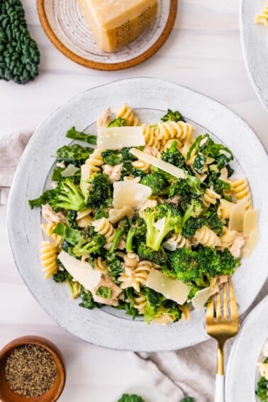 Tuna, broccoli and kale caesar pasta salad on a plate topped with shaved parmesan.