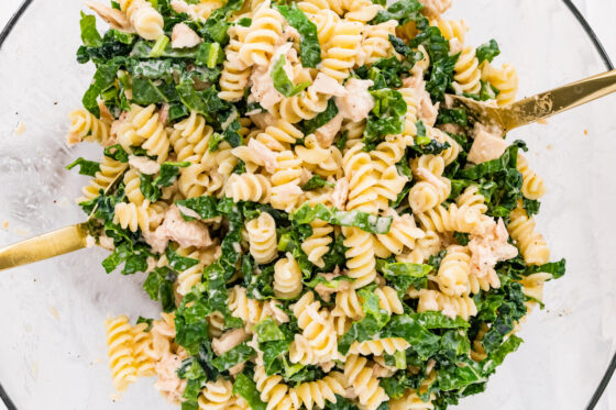 Tuna, kale, caesara dressing and pasta tossed together in a bowl.