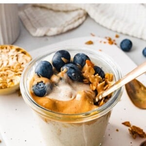 A jar of blended overnight oats topped with blueberries, nut butter and granola.