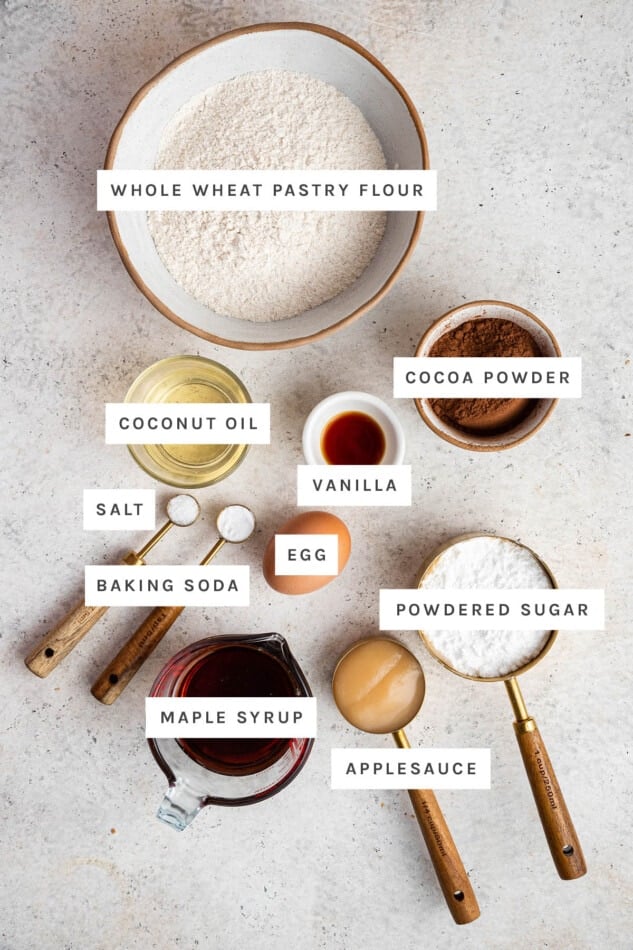 Ingredients measured out for Chocolate Crinkle Cookies: whole wheat flour, coconut oil, cocoa powder, vanilla, salt, baking soda, egg, powdered sugar, maple syrup and applesauce.