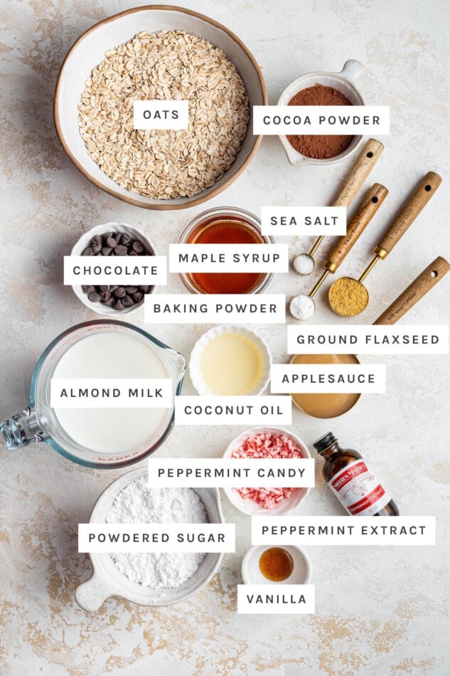 Ingredients measured out to make Chocolate Peppermint Baked Oatmeal: oats, cocoa powder, chocolate, maple syrup, sea salt, baking powder, ground flaxseed, applesauce, coconut oil, almond milk, peppermint candy, peppermint extract, powdered sugar and vanilla.