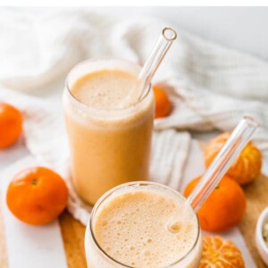 Two glasses of clementine smoothies with glass straws.