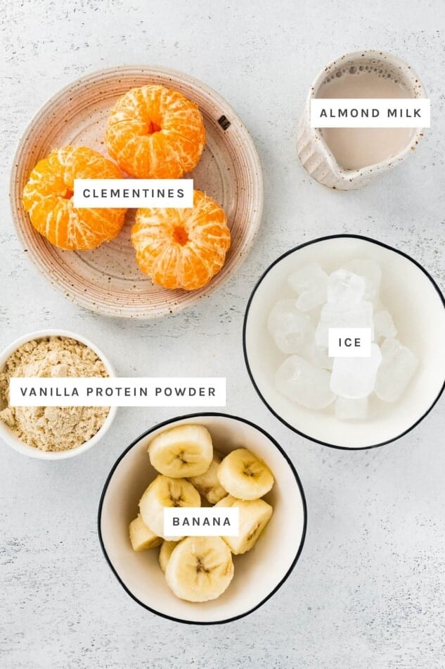 Ingredients measured out to make Creamy Clementine Smoothie: clementines, almond milk, vanilla protein powder, ice and banana.
