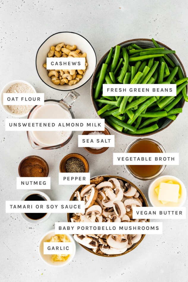 Ingredients measured out to make Healthy Green Bean Casserole: cashews, oat flour, green beans, almond milk, sea salt, pepper, vegetable broth, nutmeg, tamari or soy sauce, vegan butter, baby portobello mushrooms and garlic.