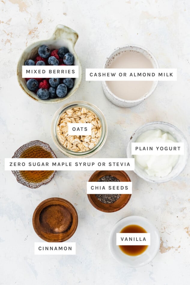 Ingredients measured out to make Low Calorie Overnight Oats: mixed berries, cashew or almond milk, oats, maple syrup, plain yogurt, chia seeds, cinnamon and vanilla.