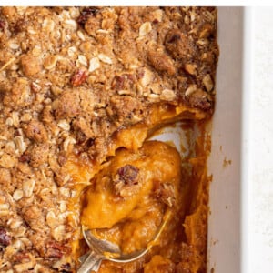A serving spoon resting in a baking dish containing healthy sweet potato casserole.