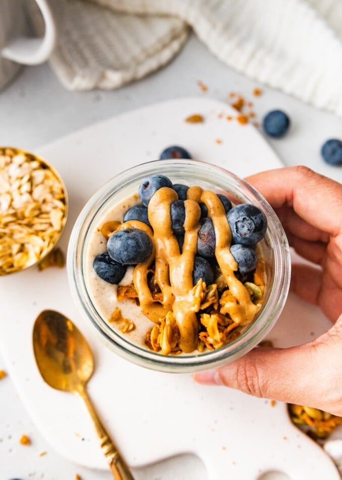 A hand holding up a jar of overnight oats.