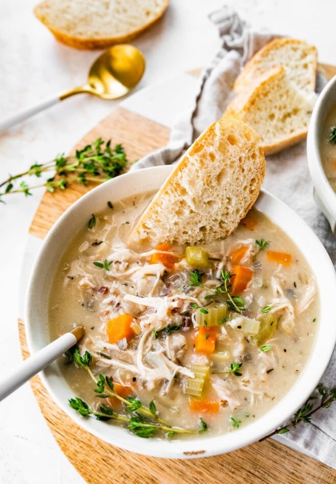 A bowl of chicken and wild rice soup with bread.