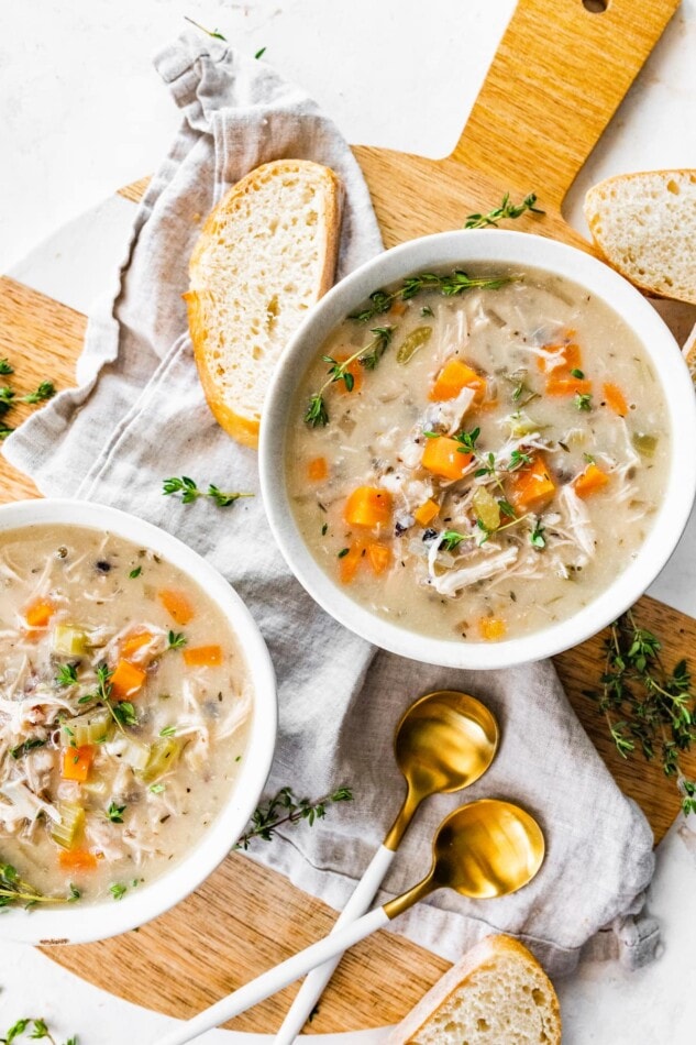 Two bowls of soup with spoons and bread.