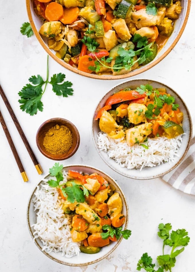Bowls of chicken curry with vegetables served with rice.