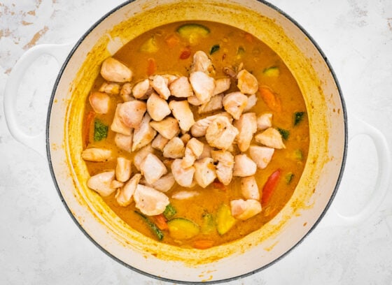 Cooked chicken added to vegetable curry in a pot.