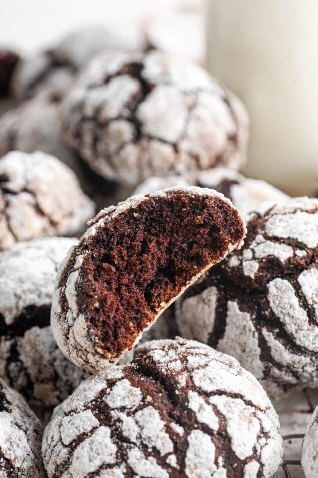 A chocolate crinkle cookie with a bite taken out of it rests on top of additional cookies.