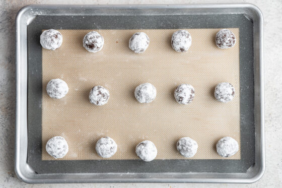 Fifteen cookie balls placed evenly across a baking sheet lined with a silpat mat.