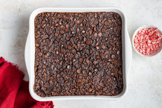 Baked oatmeal in a baking dish with a small bowl of crushed peppermints next to it.