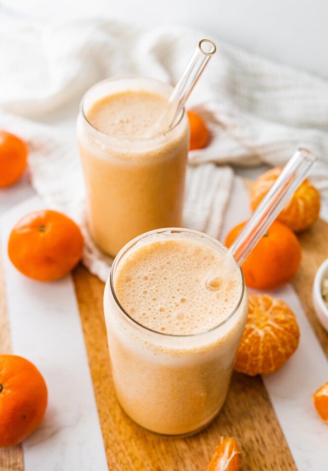 Two clementine smoothies with straws.
