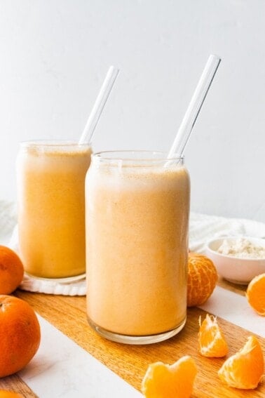 Two clementine smoothies with straws.