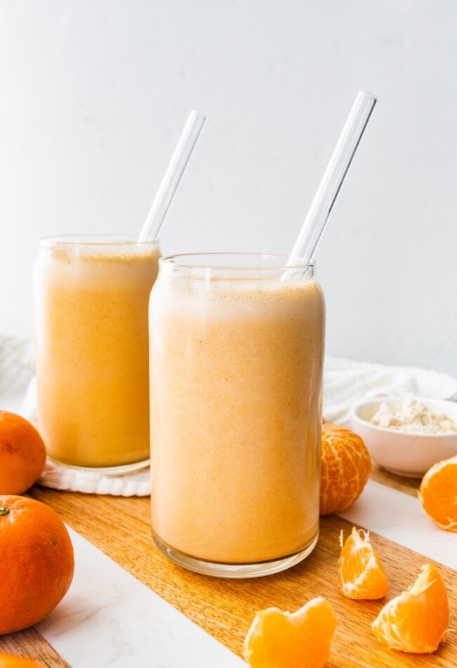 Two clementine smoothies with straws.