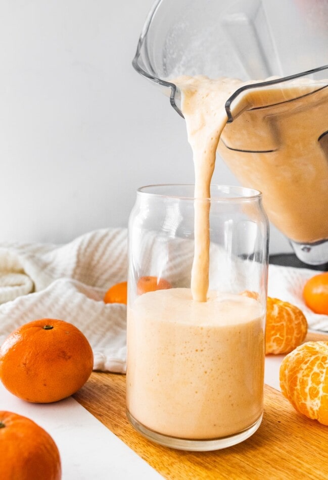 Pouring clementine smoothie into a glass.