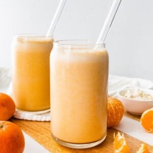 Two clementine smoothies with straws.