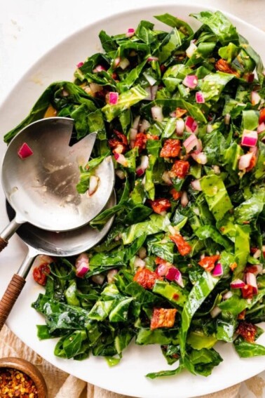 A serving bowl containing raw collard greens salad with salad servers.