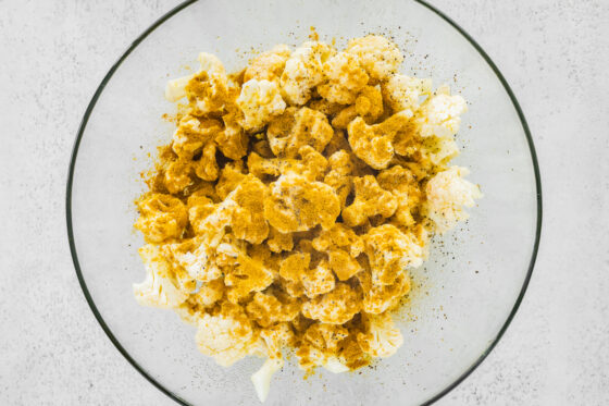 Seasonings sprinkled onto cauliflower florets in a bowl.