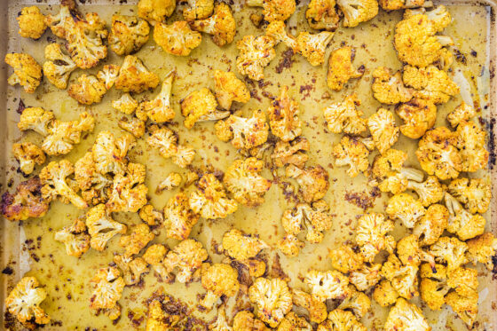 Curry roasted cauliflower spread across a parchment lined baking sheet.