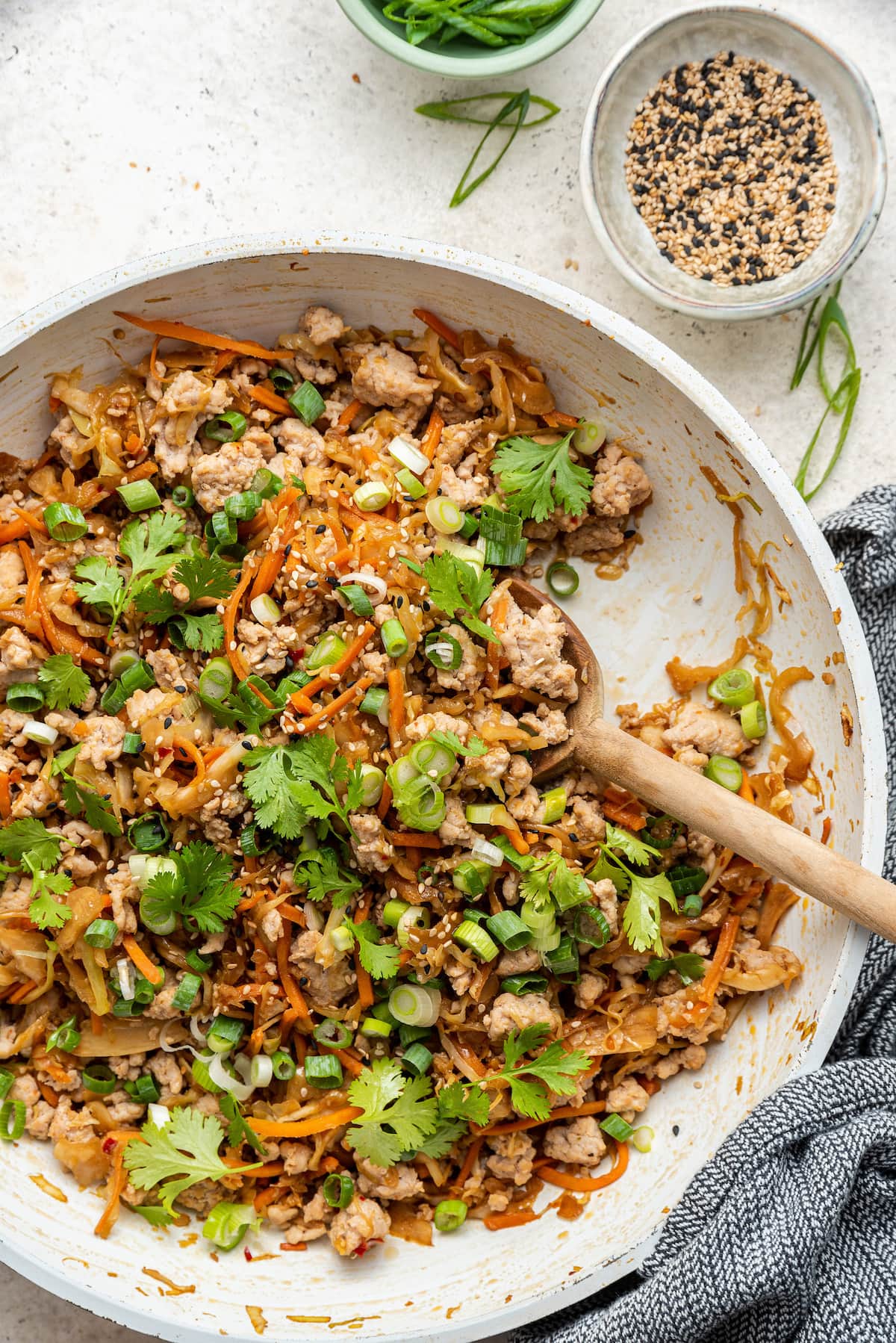 A sauté pan containing egg roll in a bowl. A wooden serving spoon rests in the pan.