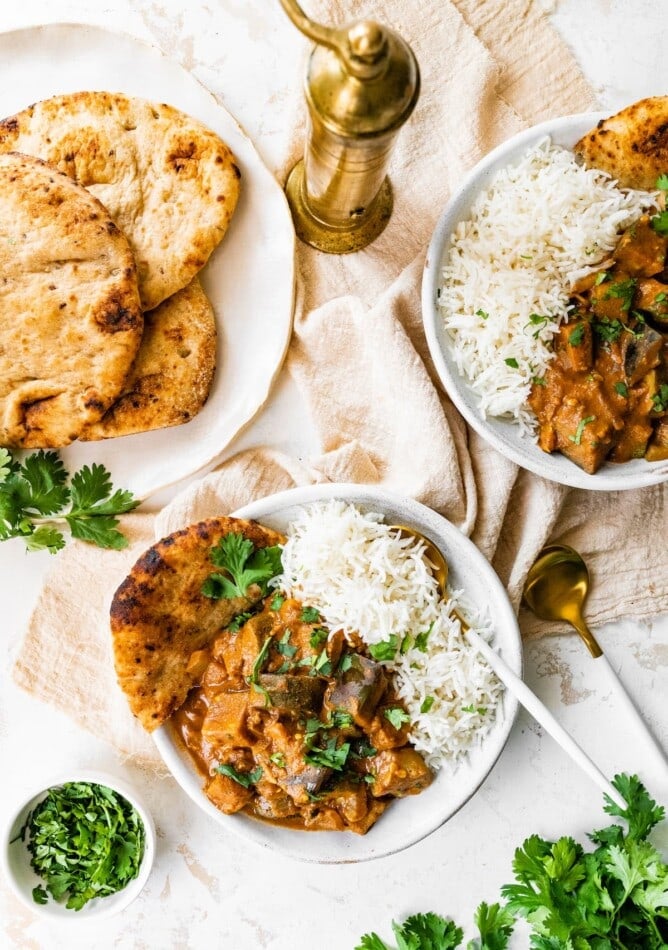 Servings of eggplant curry with rice and a plate of naan.