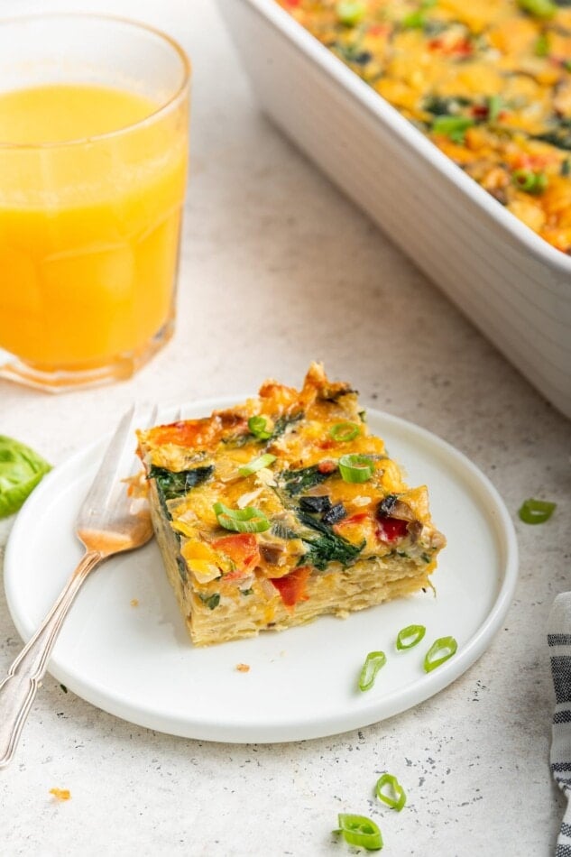 A slice of casserole on a plate with a fork and a glass of orange juice.