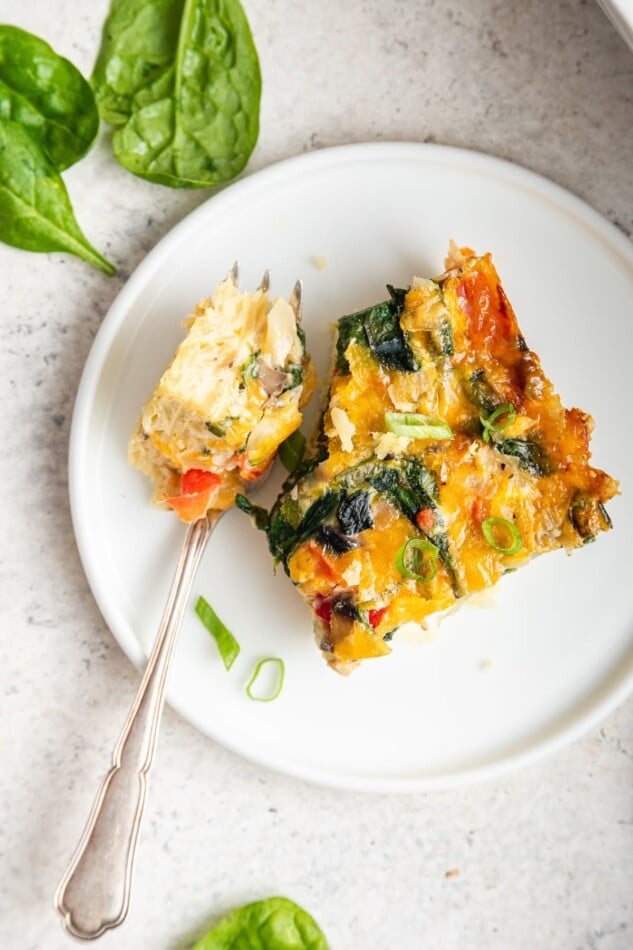 A fork with a piece of casserole on it next to a slice on a plate.