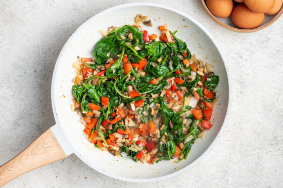 Spinach wilted with veggies in a sauté pan.