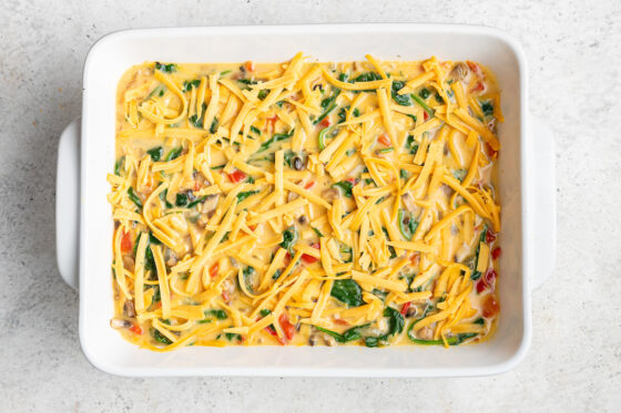 Casserole mixture added to a baking dish topped with shredded cheese.