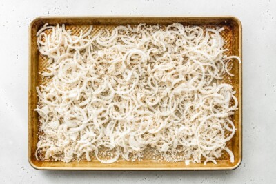 Onion slices coated in bread crumbs spread across a baking sheet.