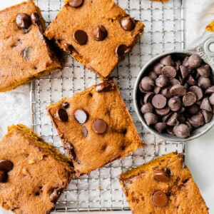 Squares of pumpkin bars on a cooling rack with a measuring cup full of chocolate chips.