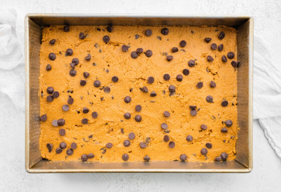 Pumpkin bar batter evenly spread across the prepared 13x9 baking pan. Extra chocolate chips are sprinkled on top.