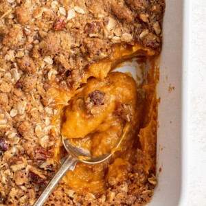 A serving spoon resting in a baking dish containing healthy sweet potato casserole.