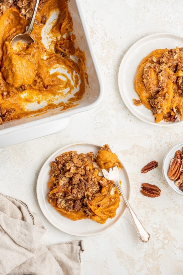 Portions of sweet potato casserole on plates next to a baking dish.