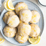 Lemon ricotta cookies on a plate with lemon wedges.