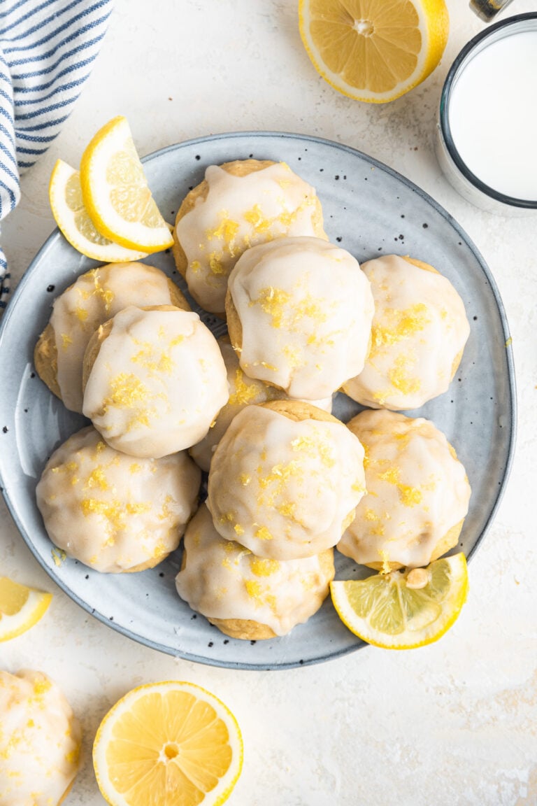 Lemon ricotta cookies on a plate with lemon wedges.