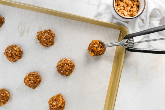 A cookie scoop scooping out cookie dough in equal portions, arranged evenly on a baking sheet.