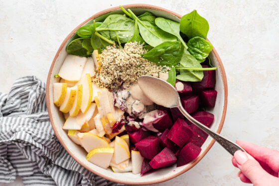 Adding dressing with a spoon to salad ingredients in a bowl.